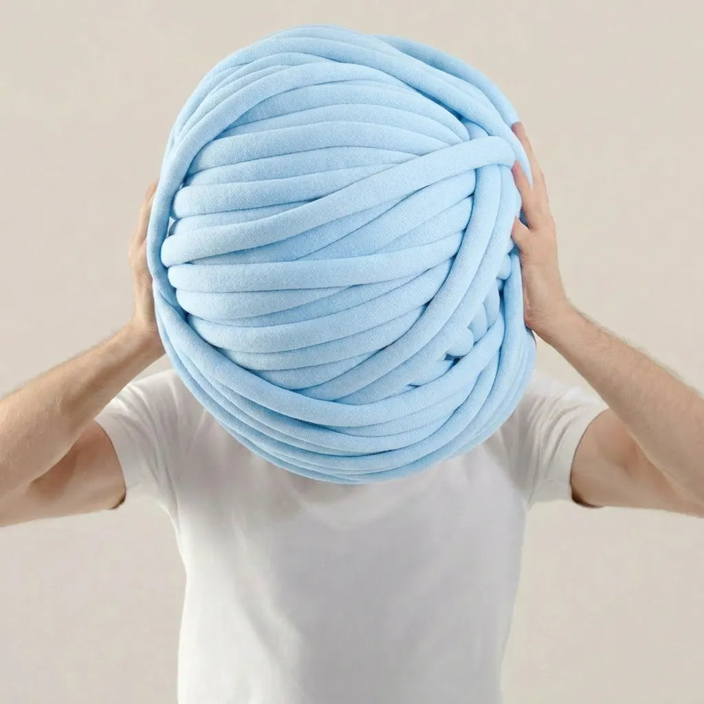 Person holding a large ball of light blue cotton tube yarn against a beige background