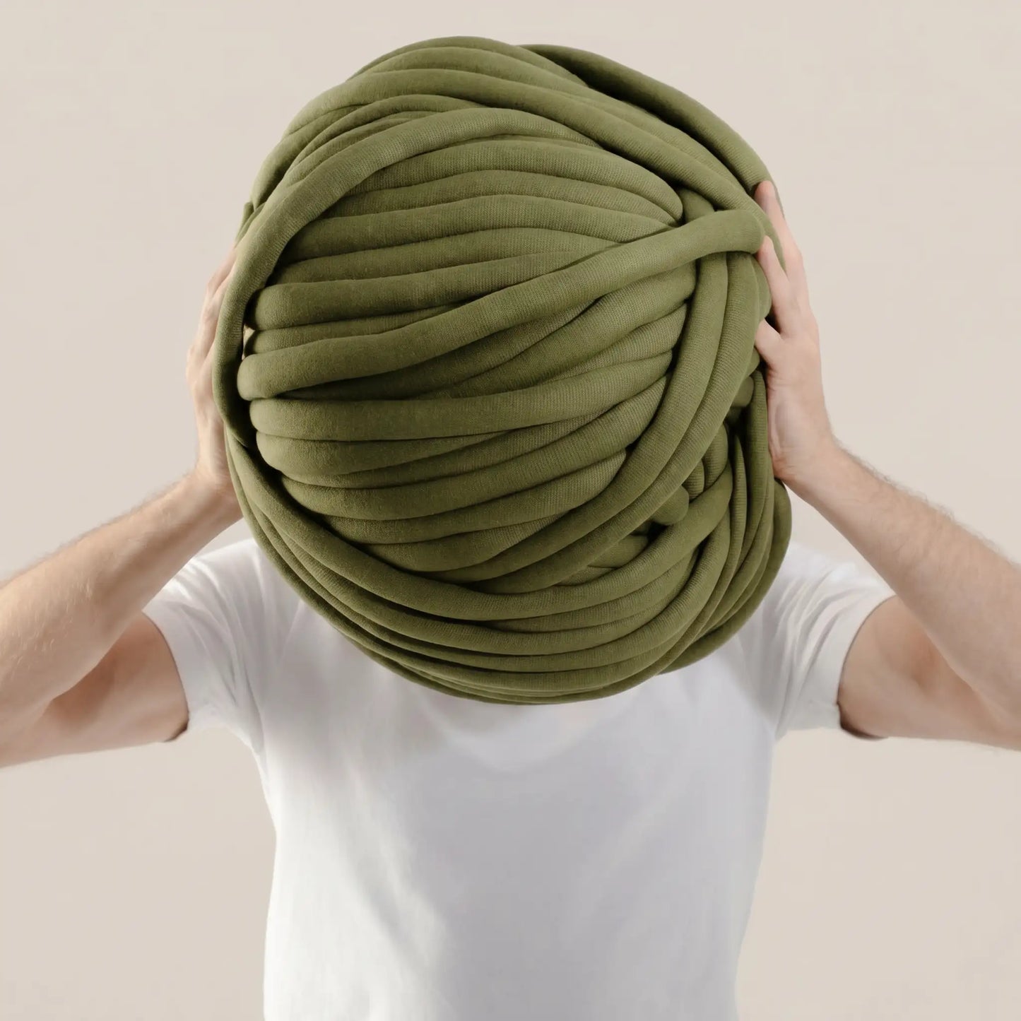 Person holding a large ball of forest green tube yarn against a beige background