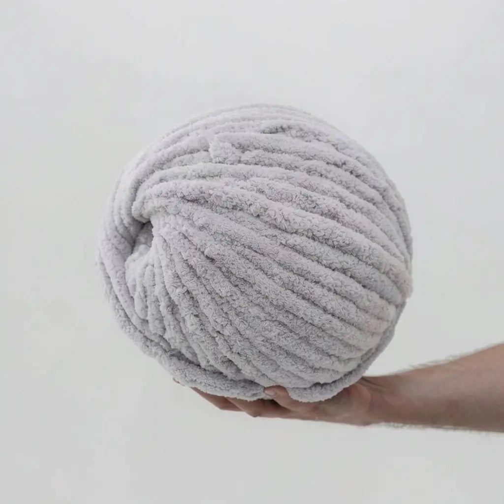 Large ball of light gray chenille yarn held by a hand against a light gray background