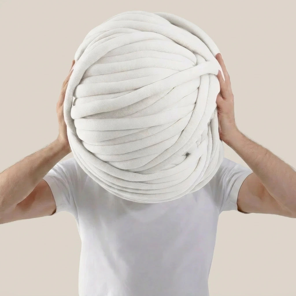 Person holding a giant ball of white tube yarn against a beige background