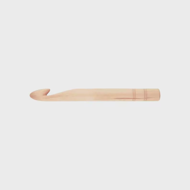 A single light natural wood crochet hook shown horizontally against a solid light gray background.