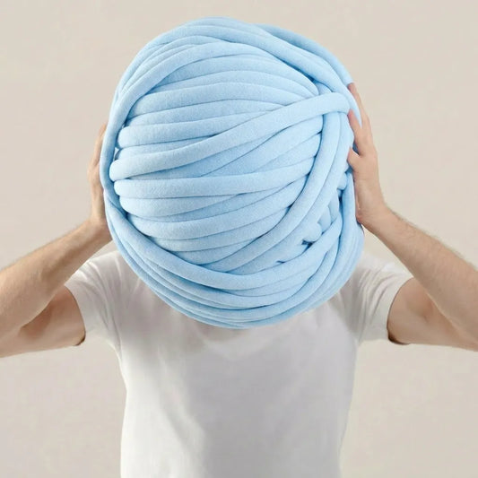 Person holding a large ball of light blue cotton tube yarn against a beige background