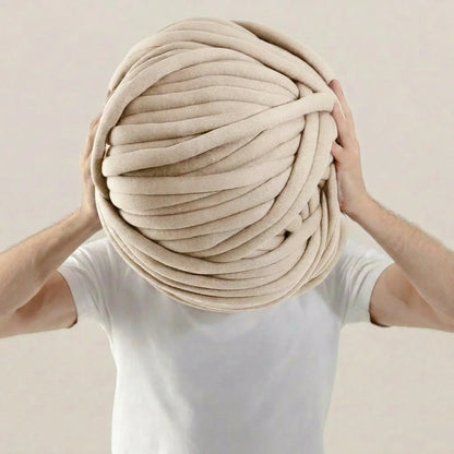 Person holding a large ball of beige tube yarn against a plain background