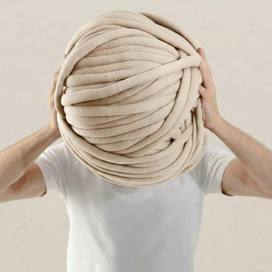Person holding a large ball of beige tube yarn against a plain background