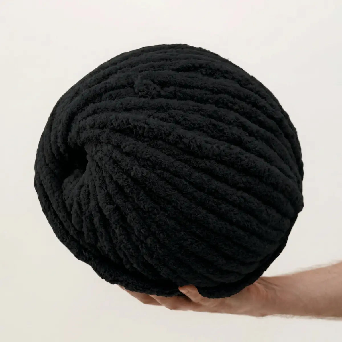 Large ball of black yarn held by a hand on a light background