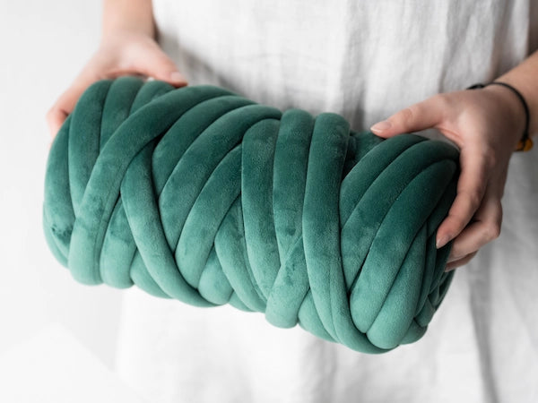 Person holding a large teal knitted ball against a white background
