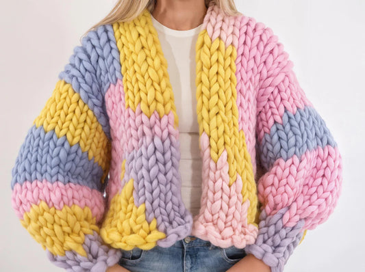 A chunky knit cardigan with large pastel stripes in pink, yellow, light blue, and lavender, worn by a model over a white top and blue jeans.