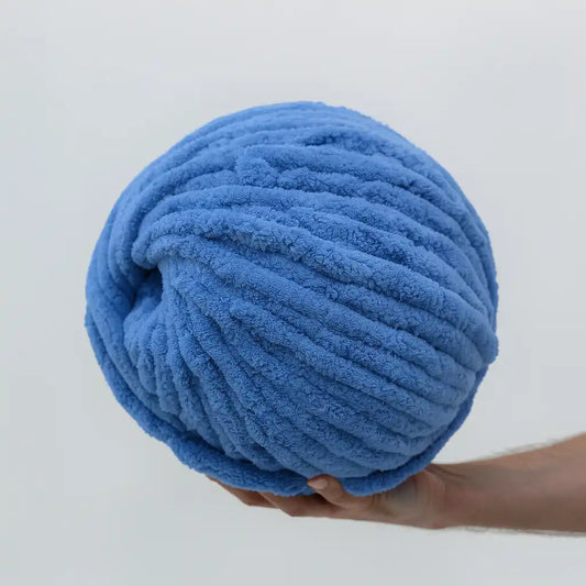 Large ball of blue yarn held by a person against a light gray background