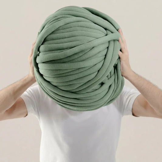 Person holding a large ball of Eucalyptus cotton tube yarn against a plain background