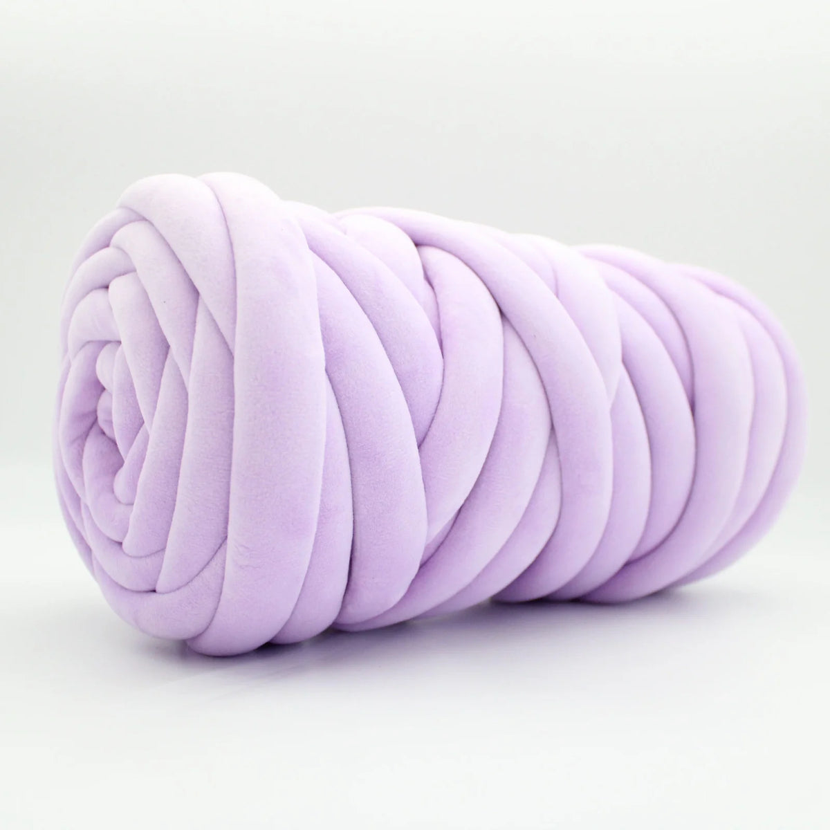 A lavender purple plush velvet tube yarn with a chunky, thick ribbed texture, rolled into a spiral shape and photographed on a clean white background.