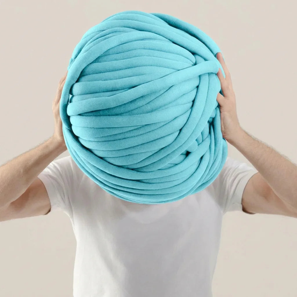 A person holding giant mint color tube yarn against plain background