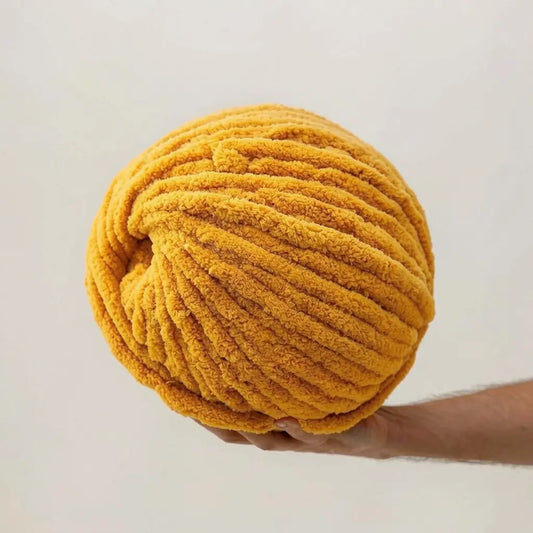 Large ball of yellow yarn held by a person against a plain background