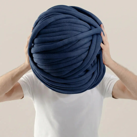Person holding a large ball of navy blue cotton tube yarn against a plain background