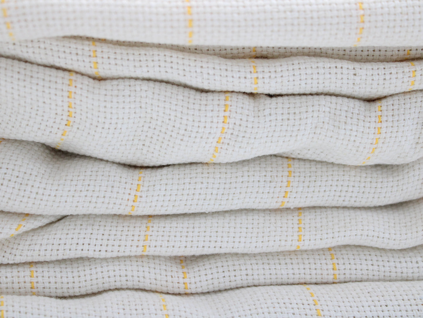 A close-up of folded tufting fabric, cotton  in a warm off-white or cream color with thin vertical yellow stripes.