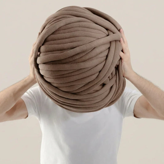 Person holding a large ball of taupe cotton tube yarn against a beige background