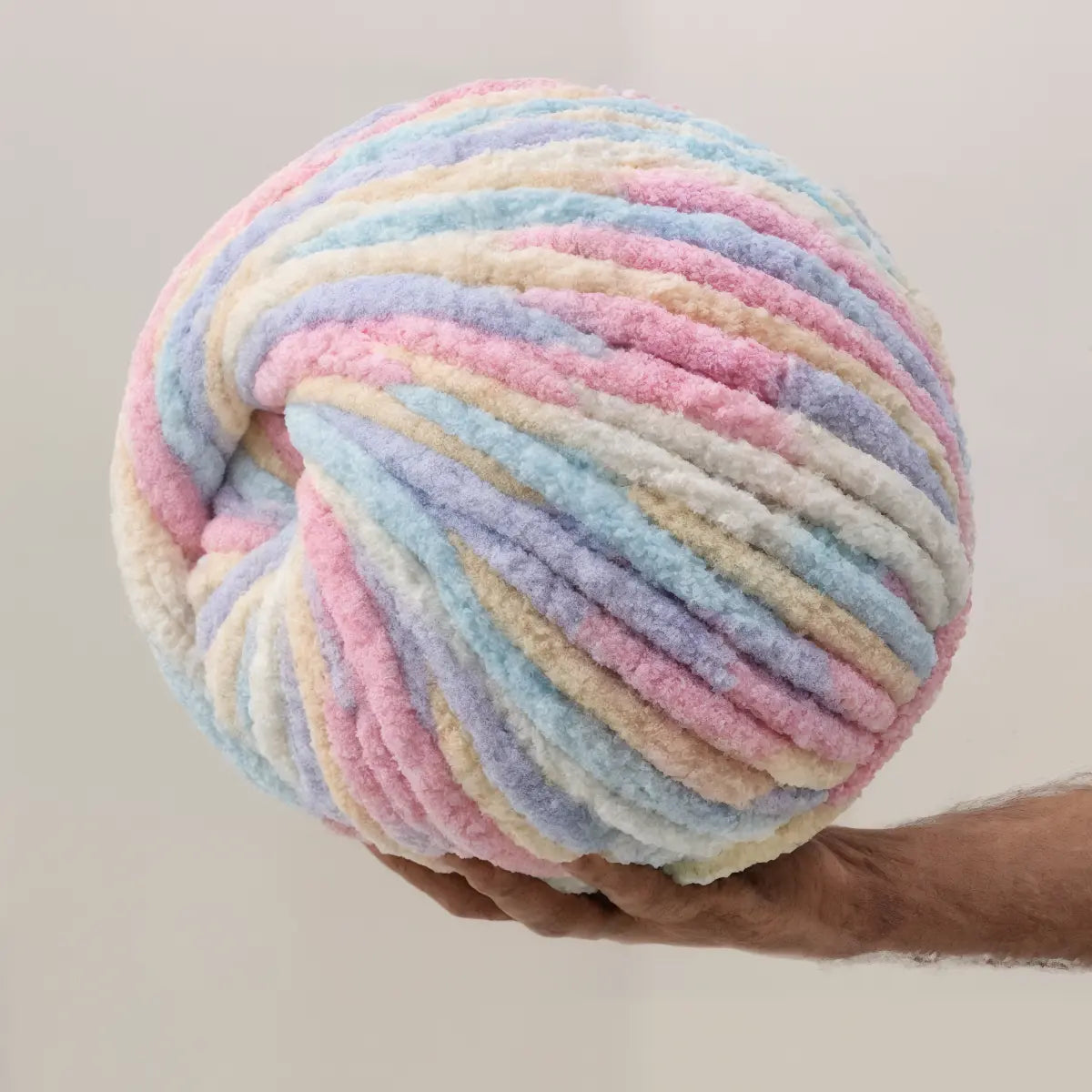 Pastel-colored yarn ball held by a hand against a neutral background