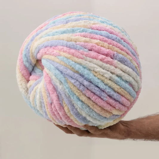 Pastel-colored yarn ball held by a hand against a neutral background