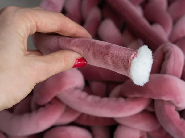 Hand holding a pink plush chunky yarn  with a white filling against a pink textured background