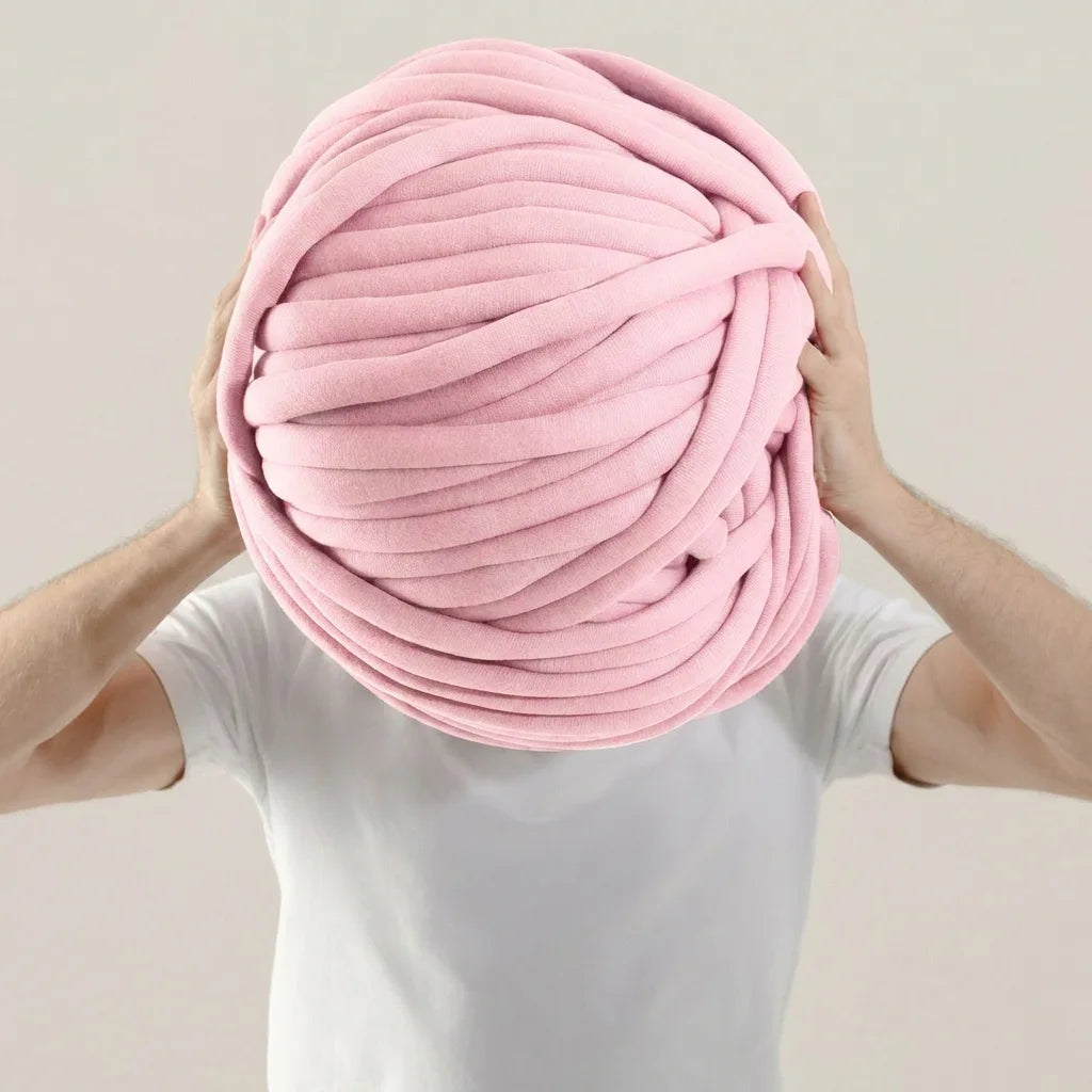 Person holding a giant baby pink cotton tube ball of yarn against a plain background