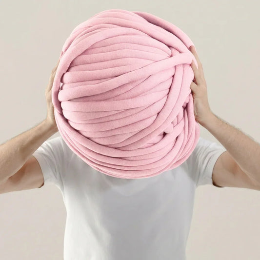 Person holding a giant baby pink cotton tube ball of yarn against a plain background