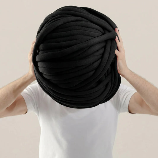 Person holding a large black cotton tube ball against a beige background