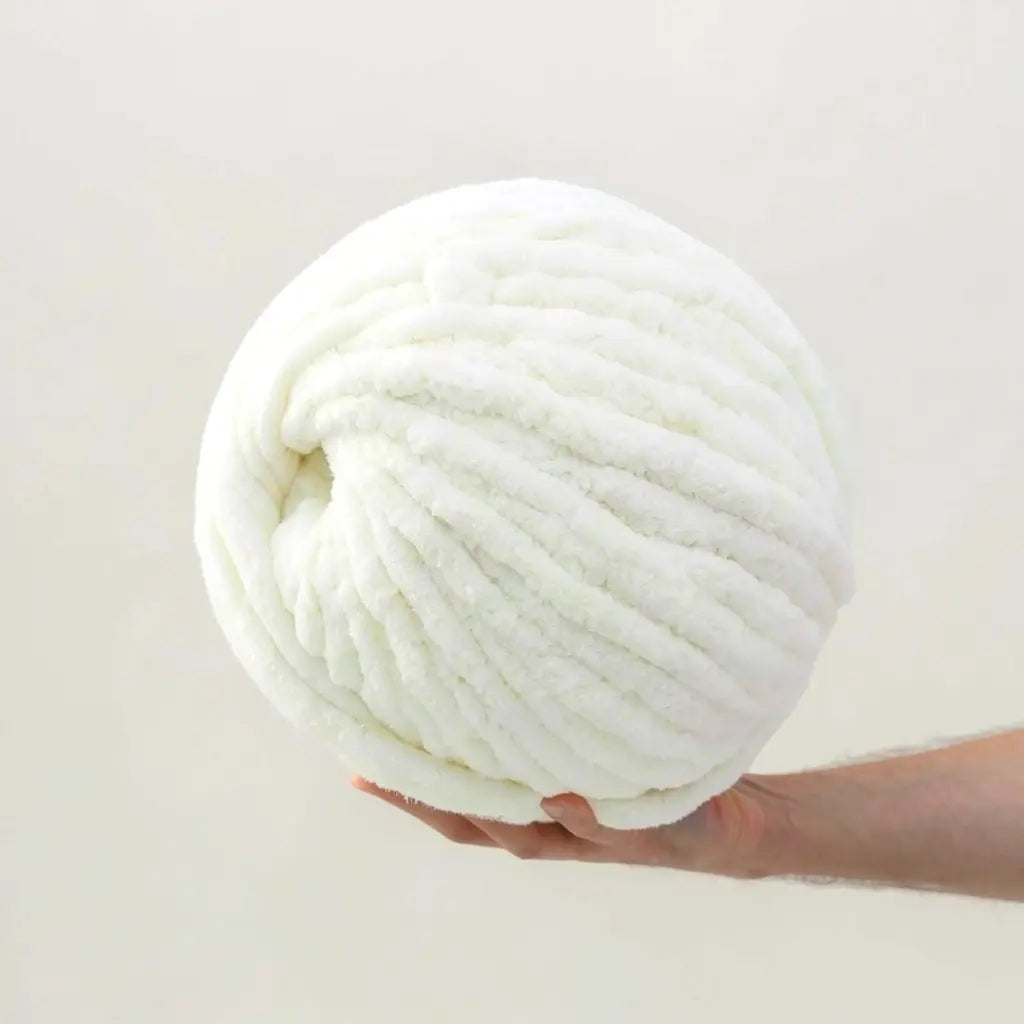 Large ball of off white chenille yarn held in a hand against a light gray background