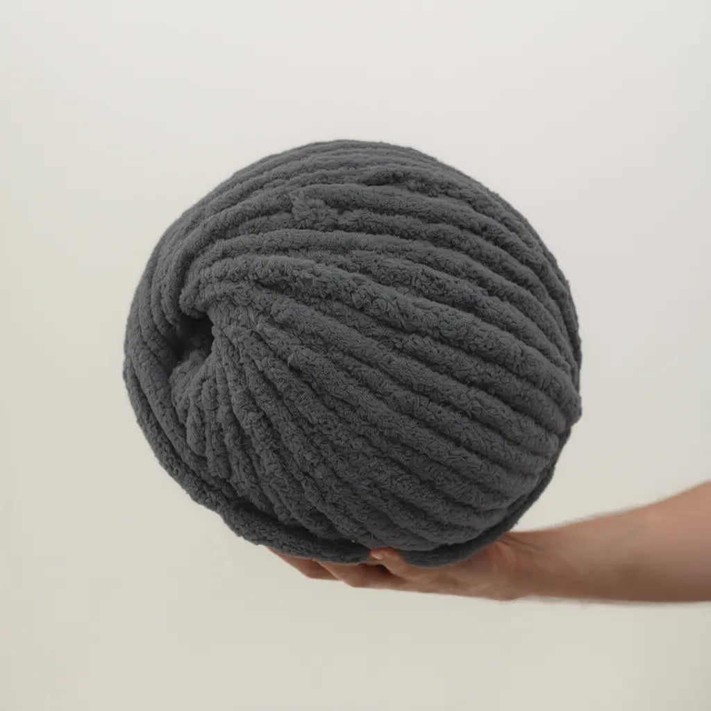 Hand holding a large chenille ball of gray yarn against a light background