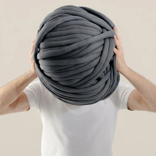 Person holding a large ball of dark gray cotton tube yarn
