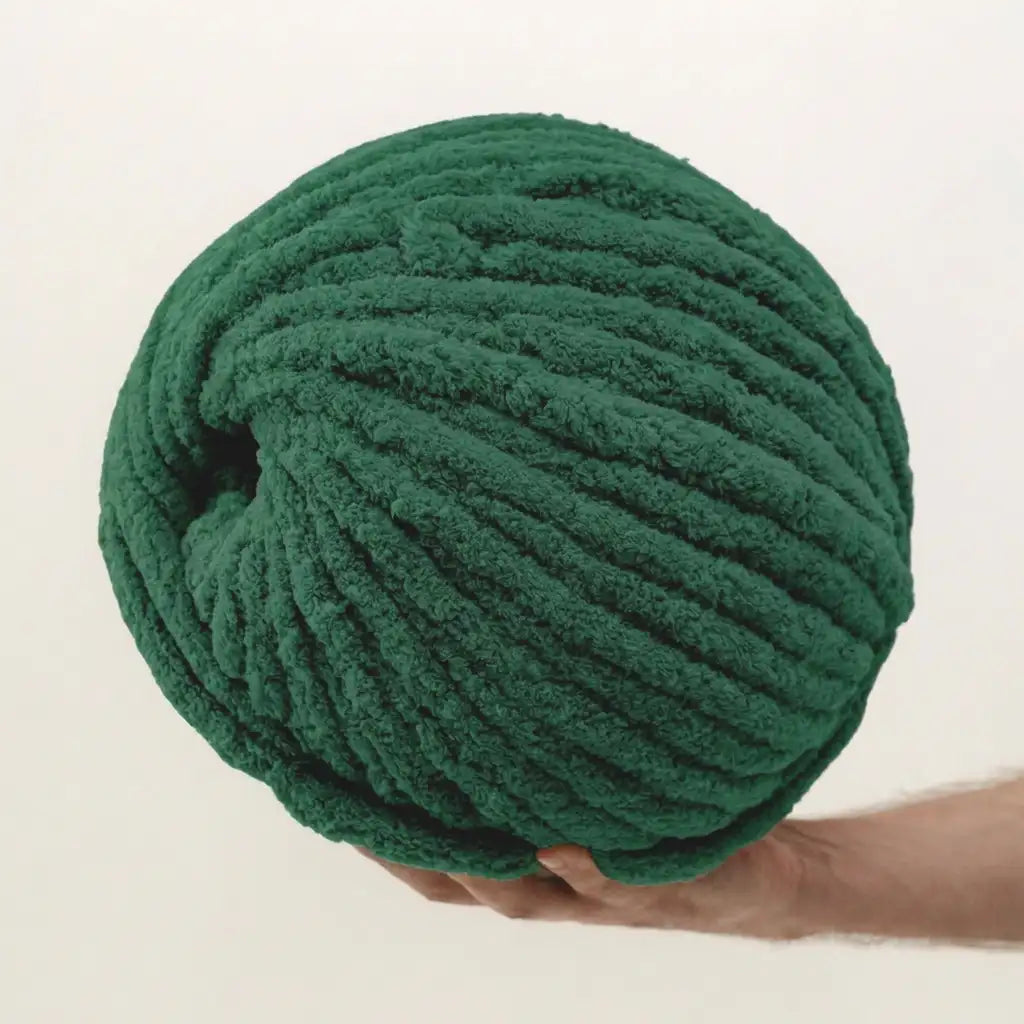 Green chenille yarn ball held by a hand on a beige background