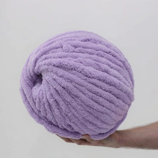 Purple yarn ball held by a hand against a light gray background