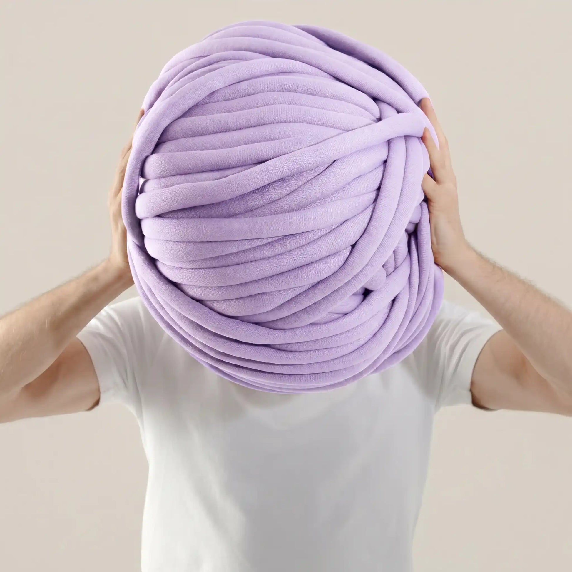 Person holding a large ball of lavender color tube yarn against a plain background