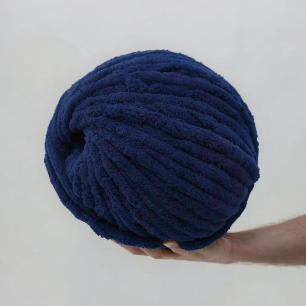 Large ball of navy blue chenille yarn held by a person against a light gray background