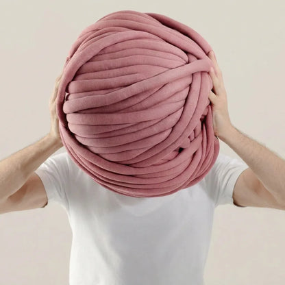 Person holding a large ball of pale pink tubular yarn against a plain background