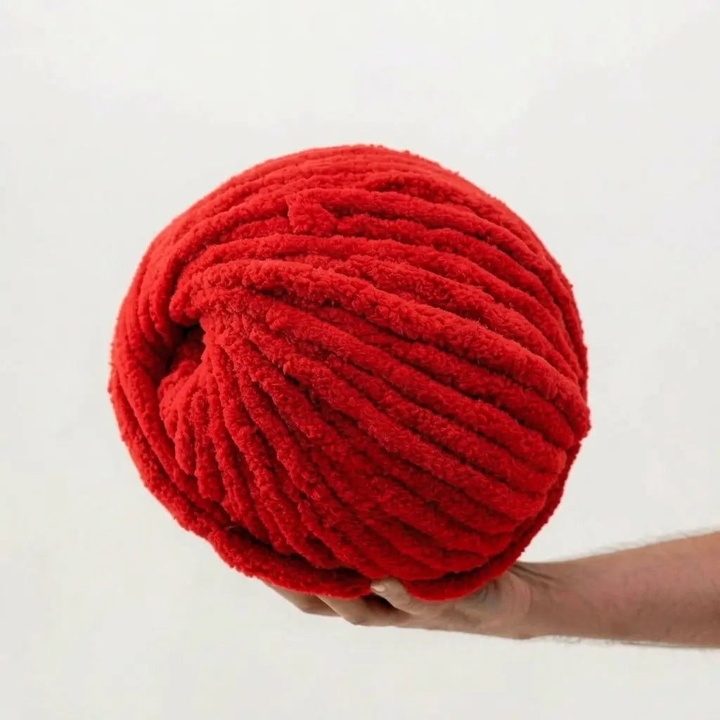 Hand holding a large ball of red chenille yarn against a white background
