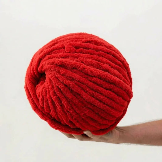 Hand holding a large ball of red chenille yarn against a white background