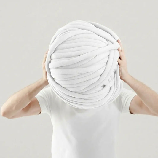 Person holding a large ball of white tubular yarn against a plain background