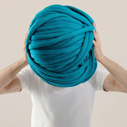 Person holding a large ball of turquoise cotton tube yarn against a plain background