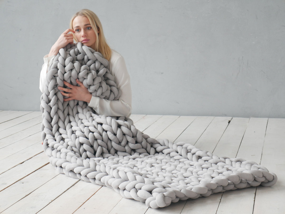 Women holding grey chunky knitted blanket in light background with wooden floors