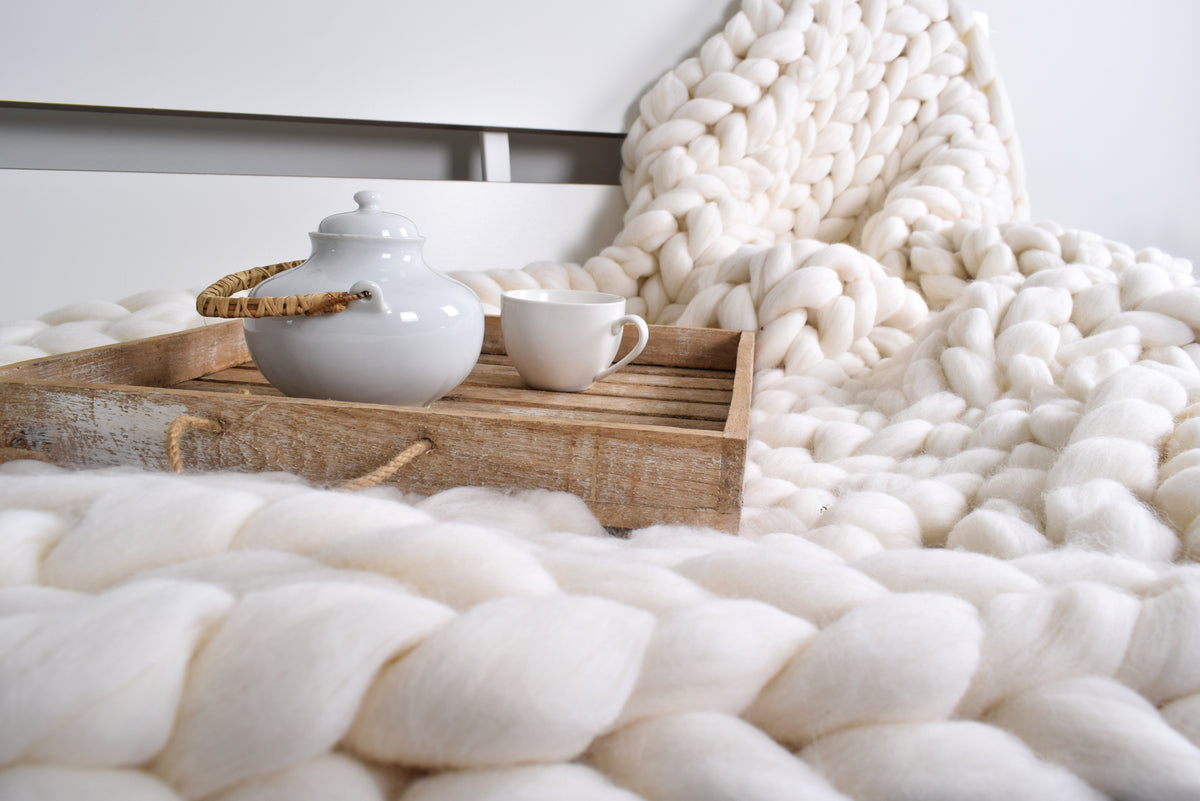 White teapot and cup on a wooden tray with a white textured chunky wool blanket in the foreground